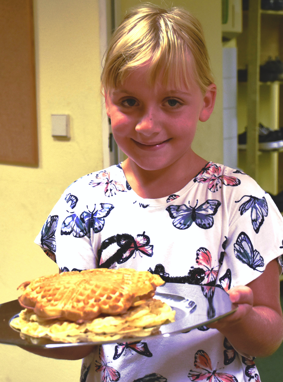 Ein lächelndes Mädchen hält einen Teller mit frisch gebackenen Waffeln
