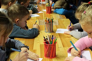Viele verschiedene Kinder sitzen an einem Tisch und malen in einem Kindergarten.