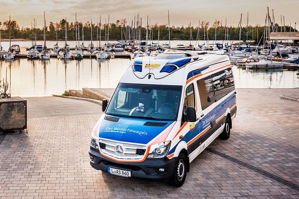 In einem Hafen steht ein Bus, der wie ein Krankenwagen aussieht, auf ihm steht jedoch: "Der Wünschewagen"