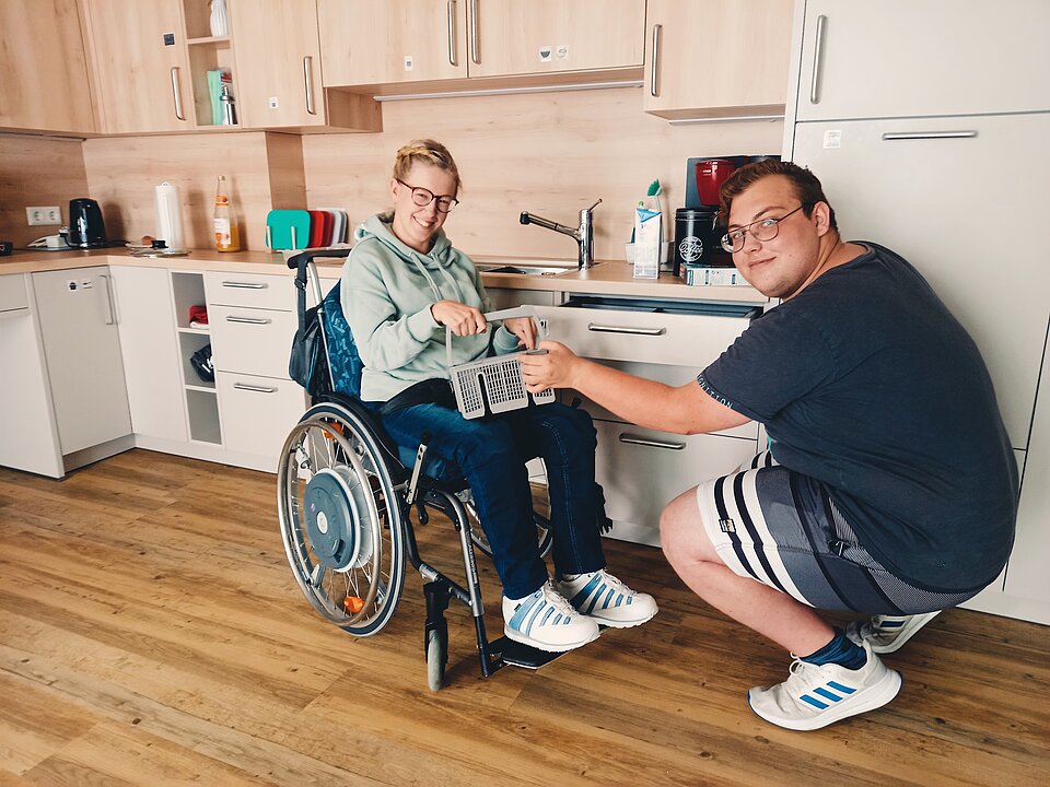 Frau im Rollstuhl mit jungem Mann bei der Hausarbeit
