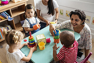 Adobe - Fachkraft mit Kindern am Tisch