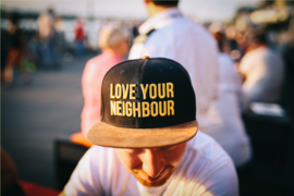 Ein Mann trägt eine Mütze, auf der trägt: "Love your Neighbour" - "Liebe deine Nachbarn"