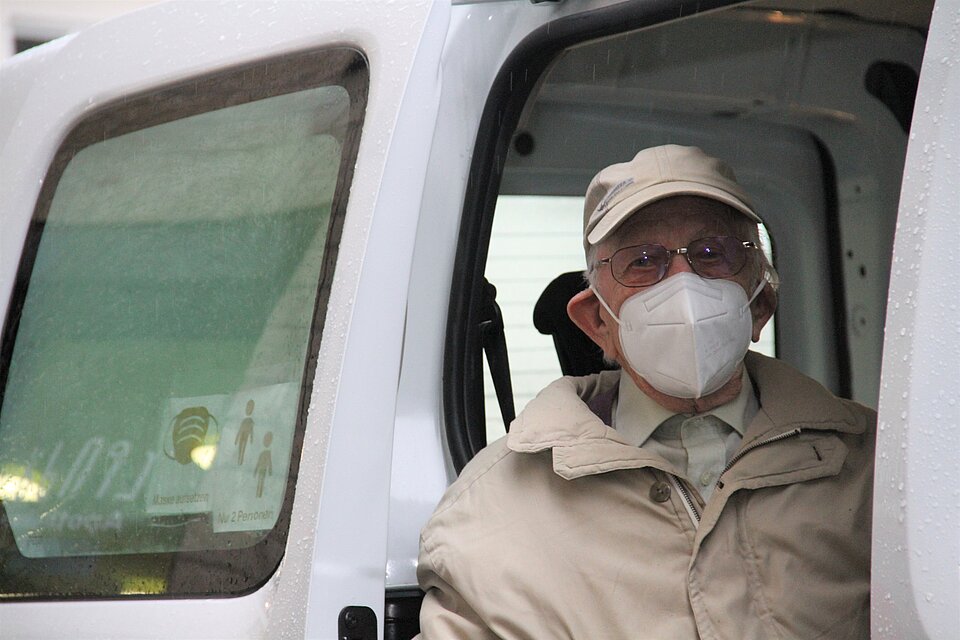 Alter Mann sitzt mit Maske im Auto