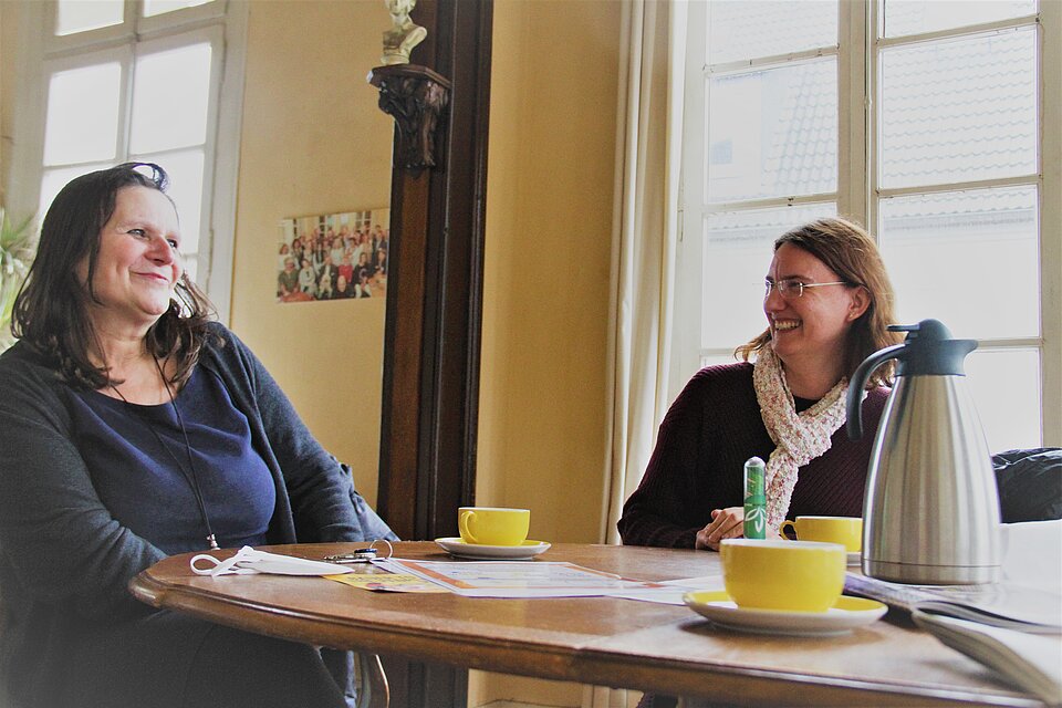 Zwei Frauen sitzen an einem Tisch und lachen sich an. 