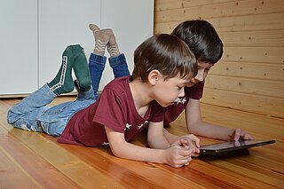 Zwei Kinder liegen auf dem Boden und schauen interessiert auf ein Tablet
