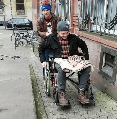 Junger Mann im Rollstuhl wird von jungem Mann geschoben