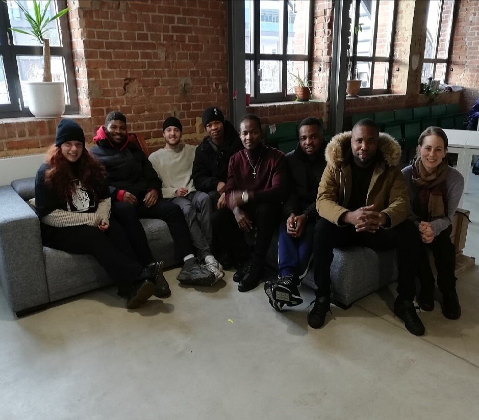 Eine Grupper junger Menschen sitzt auf einer Couch. Einige sind schwarz, andere weiß, alle lächeln.