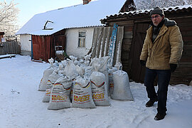 Ein Mann steht im Winter im Schnee vor Säcken mit Heizmaterialien, auf denen "Arbeiter-Samariter-Bund" steht.