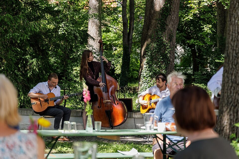 Drei Personen musizieren für Publikum in einem Garten