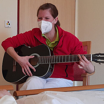 Ergotherapeutin spielt am Bett eines Bewohners Gitarre