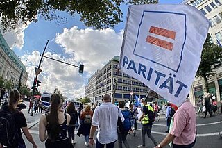 Menschen auf einer Demonstration, eine Person trägt eine Fahne mit der Aufschrift "Parität"