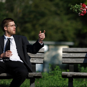 Bräutigam sitzt auf Parkbank und wirft Blumenstrauß